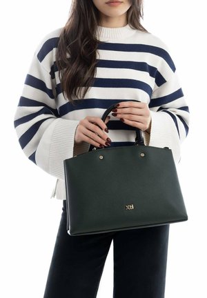 Bolso tote de cuero verde con herrajes y logo dorados, con forma estructurada y asas dobles. Usado con un suéter de rayas azul marino y blanco.