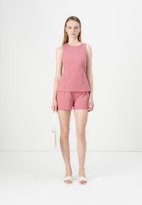 Conjunto de top sin mangas y pantalones cortos en patrón de cuadros rojo y blanco, hecho de una tela ligera, combinado con un bolso blanco y sandalias.