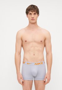 Svijetlosivi Nike bokserice s narančastim pojasom, s uskim krojem i glatkom teksturom. Dizajn uključuje oblikovani prednji dio.