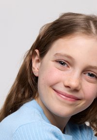 Srebrna, serduszko w kształcie kolczyka, noszona w lewym uchu. Jasnoniebieski sweter z prążkowaną strukturą i okrągłym dekoltem. Brązowe włosy w delikatnych falach.