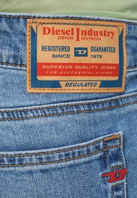 Denimpüksid, millel on pruun nahast plaastriga, millel on punane ja sinine tekst. Tagataskul on punase õmblusega detail. Klassikaline sinine pesu.