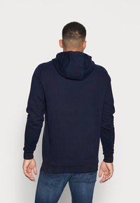 Sudadera azul marino con capucha ajustable, mangas largas y puños acanalados. Fabricada con material suave, presenta un corte holgado y un diseño sencillo.