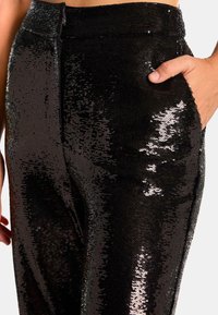 Pantalons en sequins noirs avec une texture lisse, dot és d'une coupe slim, de poches latérales et d'une ceinture. Des sequins réfléchissants créent un effet scintillant.
