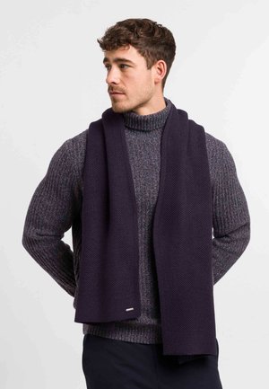 Navy knitted scarf made of thick fabric, featuring a textured pattern. Worn over a gray chunky turtleneck sweater, showing a smooth finish.
