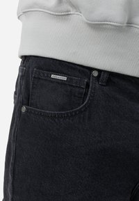 Sorte denim jeans med en tekstureret overflade, som har en forlommer og et mærketag. Matcher med en lys grå ribbet sweatshirt.