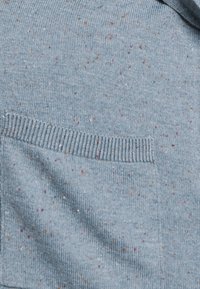 Světle modrý pletený svetr se strukturovaným vzorem a tečkami v oranžové a fialové barvě. Obsahuje vodorovnou kapsu a žebrované okraje.