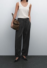 Débardeur en maille blanche avec un motif en losange, associé à un pantalon noir ample avec une taille nouée, et un sac à bandoulière en daim marron.