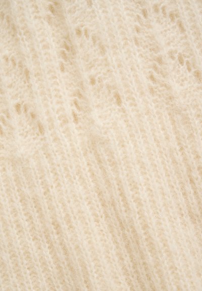 Gros plan d'un tissu tricoté doux de couleur crème avec une texture duveteuse et des motifs de couture visibles.