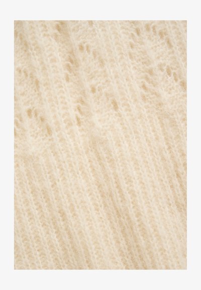 Gros plan d'un tissu tricoté doux de couleur crème avec une texture duveteuse et des motifs de couture visibles.