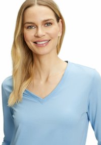 Hellblaues Langarmoberteil mit V-Ausschnitt. Glatter Stoff und taillierte Form. Minimalistisches Design, keine Muster oder Verzierungen.