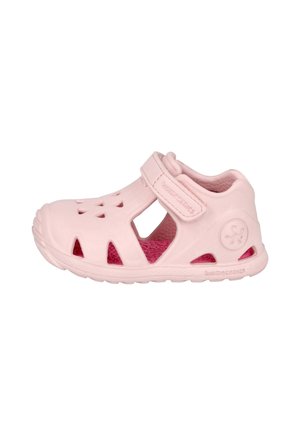 Sandalia rosa claro para niña pequeña con puntera cerrada, laterales recortados, correa ajustable de velcro y plantilla texturizada, mostrada sobre fondo blanco.