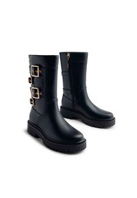 Botas negras impermeables con un acabado suave, que presentan tres hebillas en tono dorado en el lateral y un cierre de cremallera para facilitar su uso. Suela de goma gruesa.