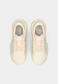 Ζευγάρι μπεζ παπουτσιών τρεξίματος Nike με ροζ κορδόνια, φωτογραφημένα από επάνω σε λευκό φόντο.