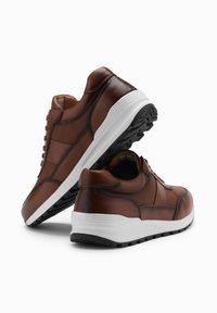 Bruine leren sneakers met een witte tussenzool, voorzien van een gestructureerde bovenkant, vetersluiting en een gepolsterde zwarte rubberen zool.