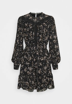 Sort langærmet blomsterkjole med beige og hvide små blomster, blonde detaljer, markeret talje, flæsekant og knaplukning i nakken bagpå.