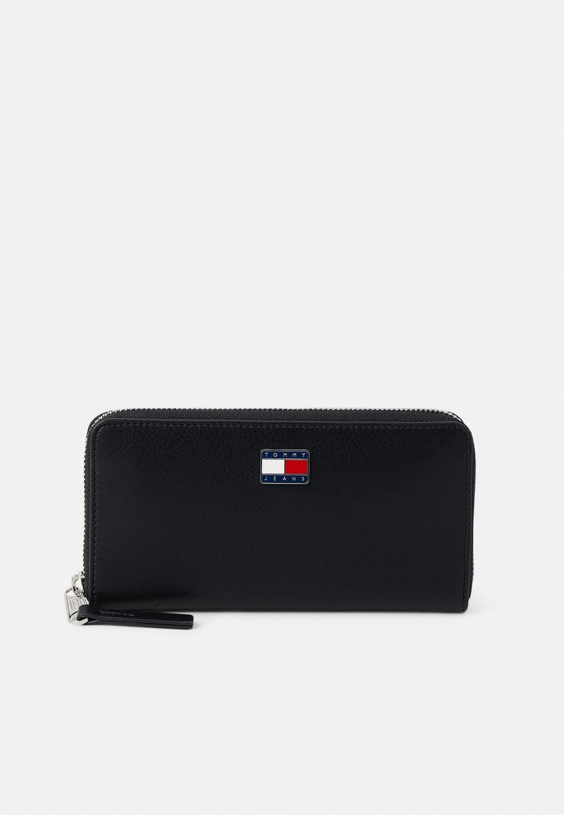 Juodas odinis piniginė su lygiu paviršiumi, užtrauktuku ir mažyiu Tommy Jeans logotipu raudonai, baltai ir mėlynai spalvų priekyje.