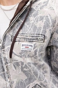 Sivi jeans jakna s bijelim i ružičastim apstraktnim uzorkom. Ima smeđi ovratnik, džep na patentni zatvarač i BDG Jeans oznaku.