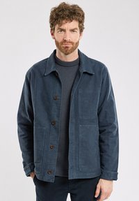 Veste bleu marine en tissu texturé, avec un col, un fermeture à boutons et deux poches avant.