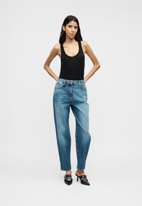 Body noir sans manches associé à un jean taille haute bleu clair. Design simple, texture en denim, et chaussures à talons hauts noires contrastantes.