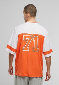 Oranžinė ir balta marškinė su trumpomis rankovėmis, ant nugaros su dideliu juodu kontūru „71“. Pagaminta iš lengvos medžiagos.