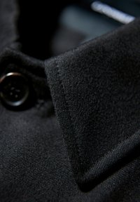 Svart skjortkrage med en texturerad tyg, som har en blank svart knapp. Närbild som framhäver detaljer och sömnad.