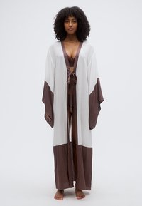 Μακρύ λευκό κιμονό με καφέ λεπτομέρειες και ζώνη στη μέση. Κατασκευασμένο από ελαφρύ ύφασμα με φαρδιά μανίκια και ανοιχτό μπροστινό σχέδιο.