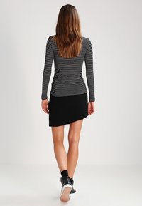 Maglietta a maniche lunghe a righe in bianco e nero, abbinata a una gonna nera asimmetrica; visibili sneakers nere alte alla caviglia.