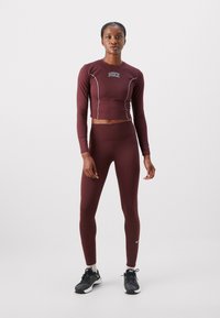 Marron cropped toppi pitkähihaisilla hihoilla, valkoisilla reunoilla ja logolla; yhteensopivat marron korkea vyötäröiset leggingsit; mustat lenkkarit valkoisella pohjalla.