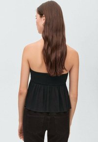 Black strapless top with a smocked bodice and a flared hem. Textured fabric with a relaxed fit. Paired with dark fitted pants.