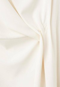 Soft cream-colored fabric twisted at the center, creating gentle folds and texture on a smooth, light background.