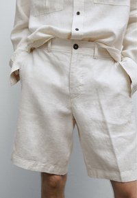 Shorts di lino beige con taglio dritto, dotati di cintura con bottone e tasche laterali. Tessuto testurizzato con una finitura naturale.