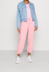Light blue denim jacket over a pink sweatshirt matching tapered sweatpants, paired with white athletic shoes. Striped pattern on the top.
