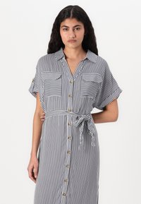 Φόρεμα με κουμπιά σε ναυτικό και λευκές ρίγες, κοντά μανίκια, δύο τσέπες στο στήθος, με ζώνη στη μέση και χρυσά κουμπιά. Λεπτό ύφασμα.