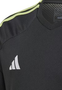 Camiseta atlética negra con escote en V, que presenta franjas de acento verde claro y un logo blanco de Adidas en la parte frontal. Tejido suave que absorbe la humedad.