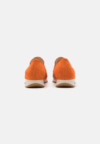 Orange suede shoes with a low heel and beige sole, featuring a smooth texture and rounded design. Back view highlights stitching details.
