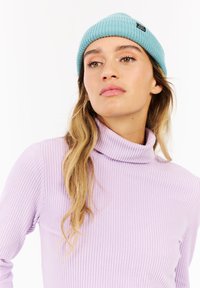 Bonnet côtelé bleu clair avec une étiquette noire, associé à un pull col roulé côtelé lavande. Vue rapprochée des deux vêtements.