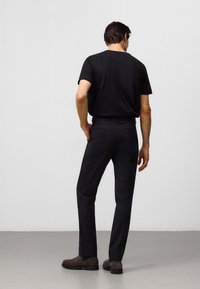 Czarna koszulka, czarne dopasowane spodnie i brązowe buty. Dopasowany krój, gładka faktura i dwie tylne kieszenie w spodniach. Widok z tyłu.