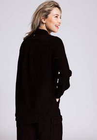 Schwarzes Cordhemd mit langen Ärmeln, durchgeknöpftem Kragen und feiner Rippstruktur. Verfügt über einen abgerundeten Saum und Seitentaschen.