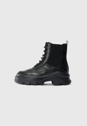 Svart lærkampboot med tykk såle, elastisk panel på siden, snøring foran og bærehank på enkel hvit bakgrunn.