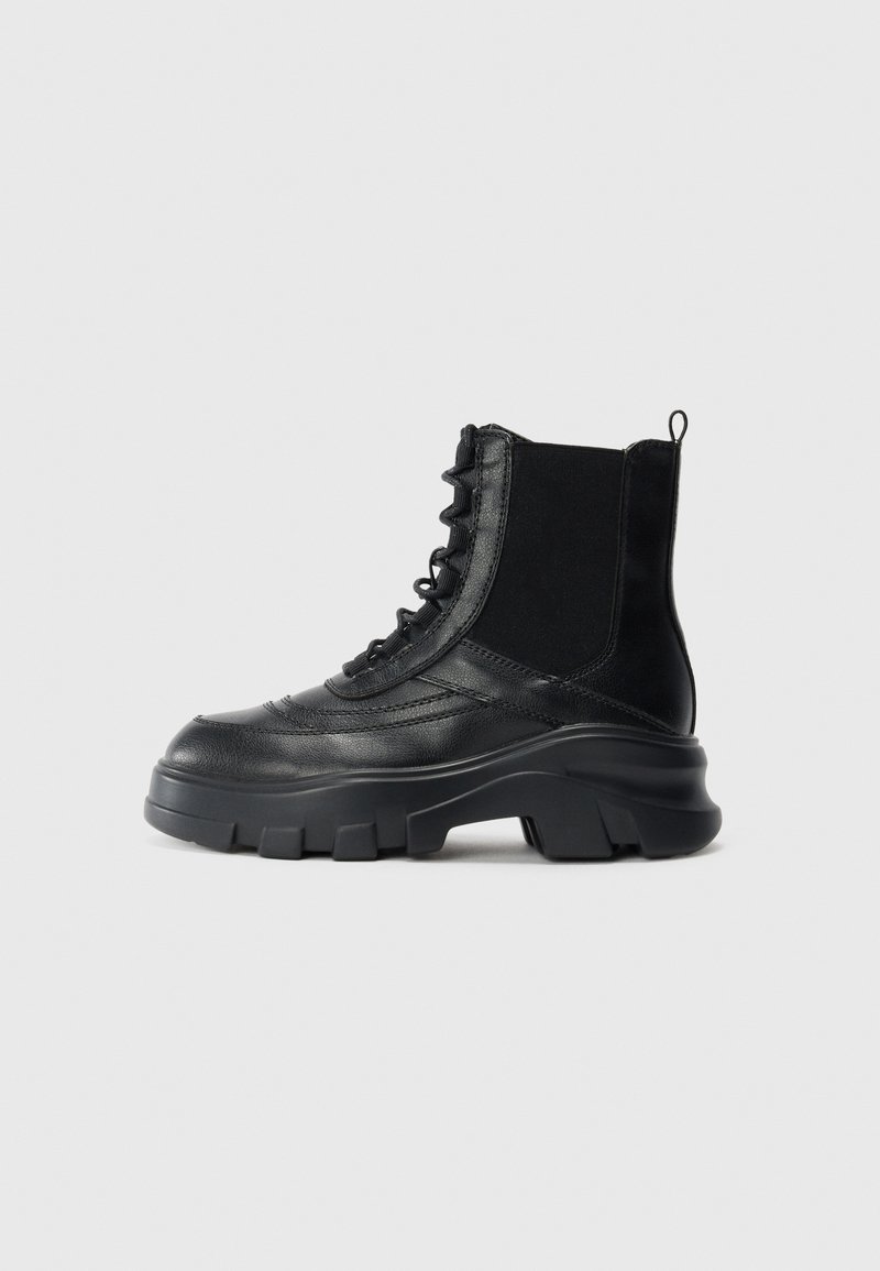 Black leather combat boot with thick lug sole, side elastic panel, lace-up front, and pull tab on plain white background.