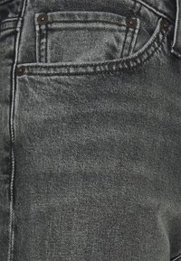 Tmavě šedé džíny z denimu mají hladkou texturu, klasický design s pěti kapsami a kovové nýty, které ukazují vybledlý vzhled pro opotřebovaný efekt.