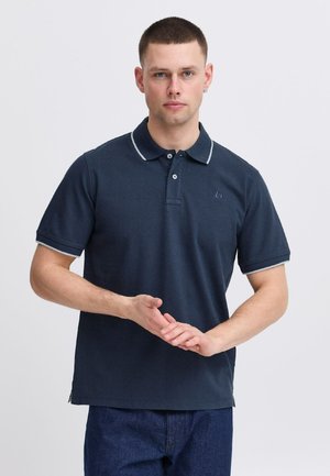 Mørkeblå polo-shirt lavet af tekstureret stof, med kontrasterende lyseblå krave og ærme-detajler, samt et logo på venstre bryst.
