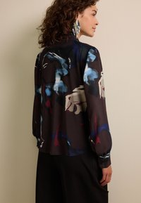 Blouse met lange mouwen in donkere stof met abstracte kleurrijke patronen. Voorzien van een kraag, knoopmanchetten en een losse pasvorm.