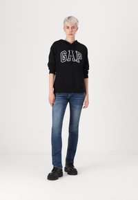 Black hooded sweatshirt with "GAP" logo, paired with fitted blue jeans and black platform shoes. Simple design and casual style.
