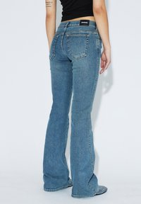 Modré džíny s rozšířenými nohavicemi a středním praním, s knoflíkovým zapínáním, pěti kapsami a černou nášivkou na zadním pásu.