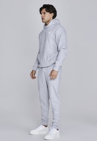 Gray cotton hoodie with front pocket and drawstring, paired with matching gray sweatpants and white sneakers, standing on a neutral background.