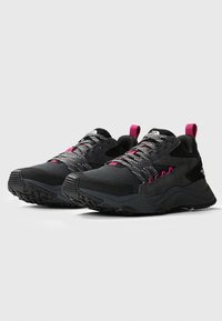 Scarpe sportive nere con dettagli rosa, dotate di una tomaia in rete e sintetico, suola testurizzata e lacci riflettenti per migliorare la visibilità.