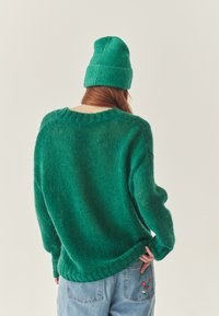 Zielony, dziany sweter o luźnym kroju i prążkowanym kołnierzu. Połączony z dopasowaną czapką, obie zrobione z miękkiego, teksturowanego materiału.