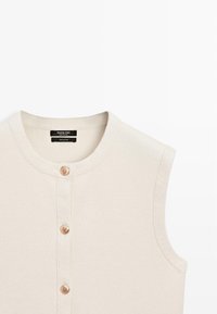 Gilet senza maniche color crema in maglia con scollo rotondo e tre bottoni dorati sulla parte anteriore.