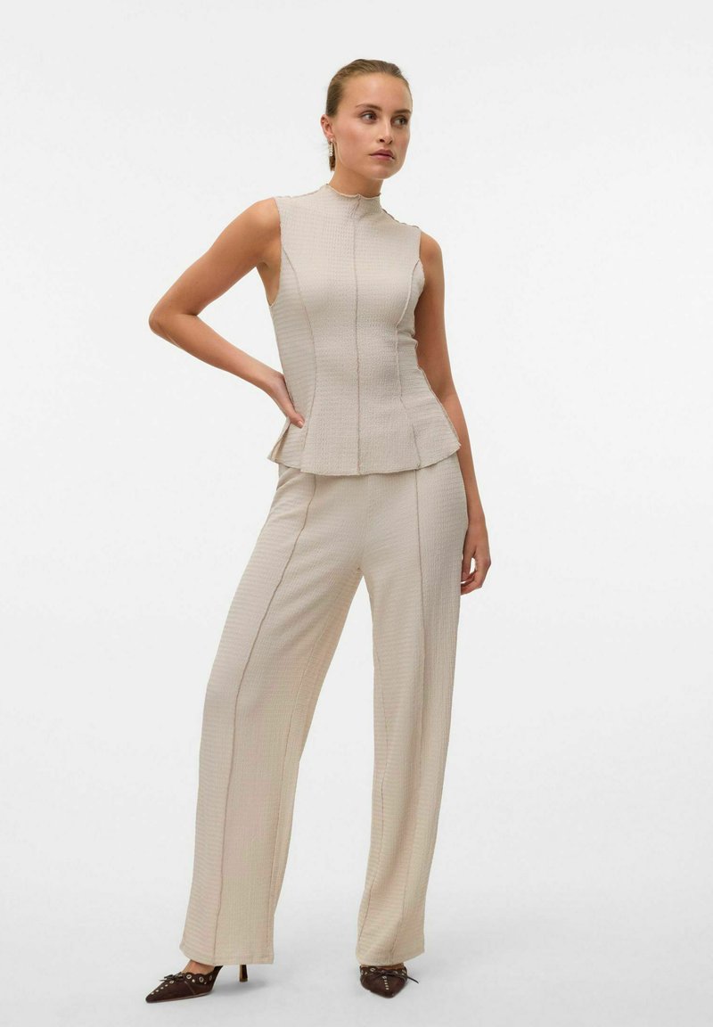 Completo beige a due pezzi composto da un top senza maniche a peplum con scollatura alta e pantaloni a gamba larga, entrambi in un tessuto testurizzato con righe verticali.